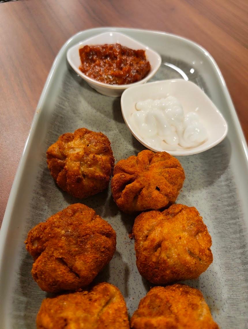 Plate of crispy fried momos with red chutney and white dip